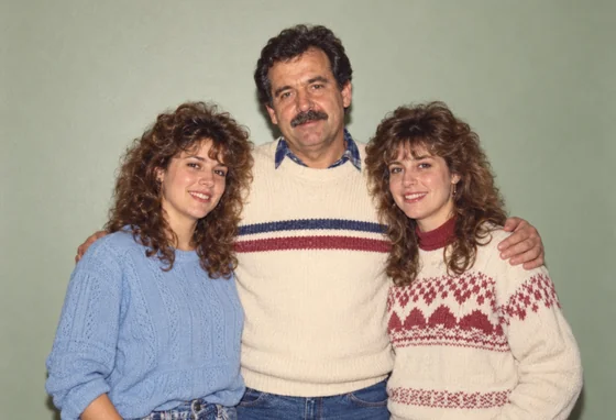 A restored color family portrait of a father and two adult daughters against a plain sage wall.