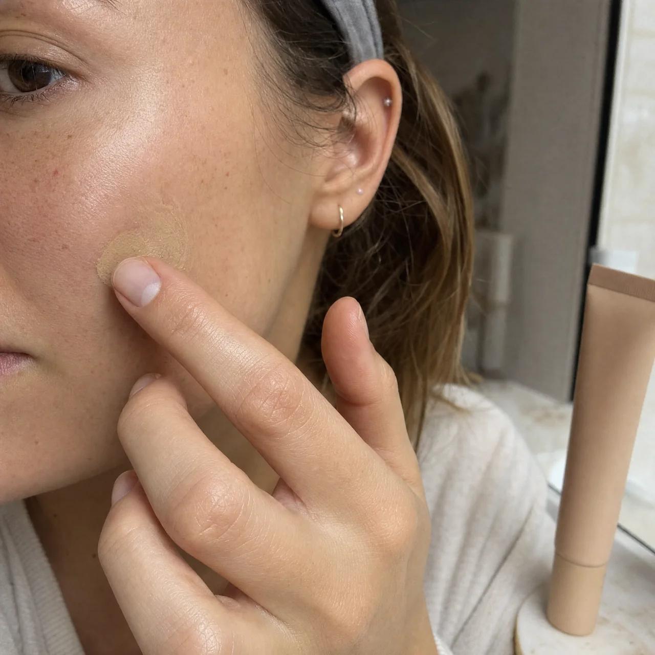 Macro close-up of a cheek as a fingertip lightly pats a thin layer of tinted moisturizer, showing skin texture and soft blended edges.