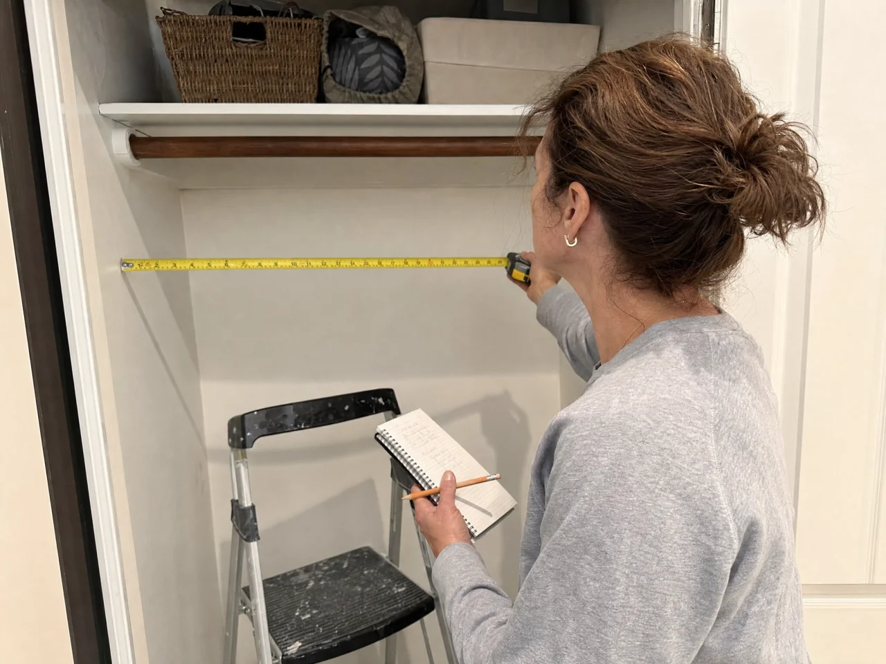 Person using a tape measure across a small closet while writing dimensions on a notepad