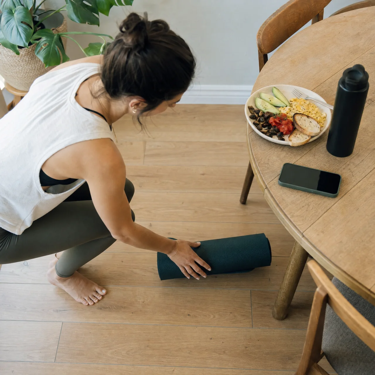 Person placing a rolled exercise mat on the floor next to a breakfast plate to link movement with a daily routine.