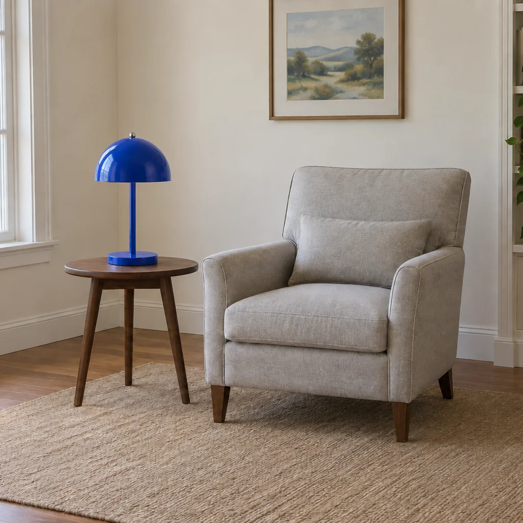 A cobalt-blue dome lamp stands on a wooden side table beside a light-gray upholstered armchair.