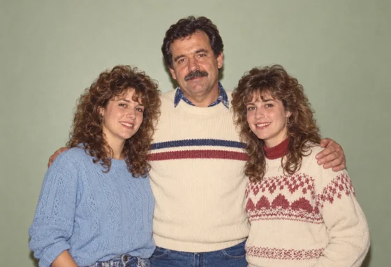 A restored color family portrait of a father and two adult daughters against a plain sage wall.